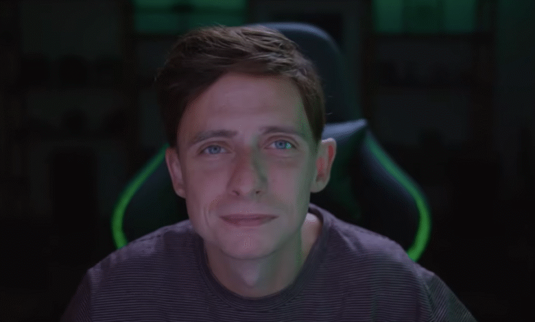 Close-up of a man with blue eyes and brown hair, smiling slightly, seated in a gaming chair with green accents.