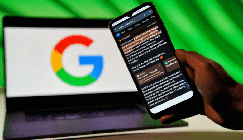 A hand holds a smartphone displaying Google AI Overviews search results next to a laptop with the Google logo.