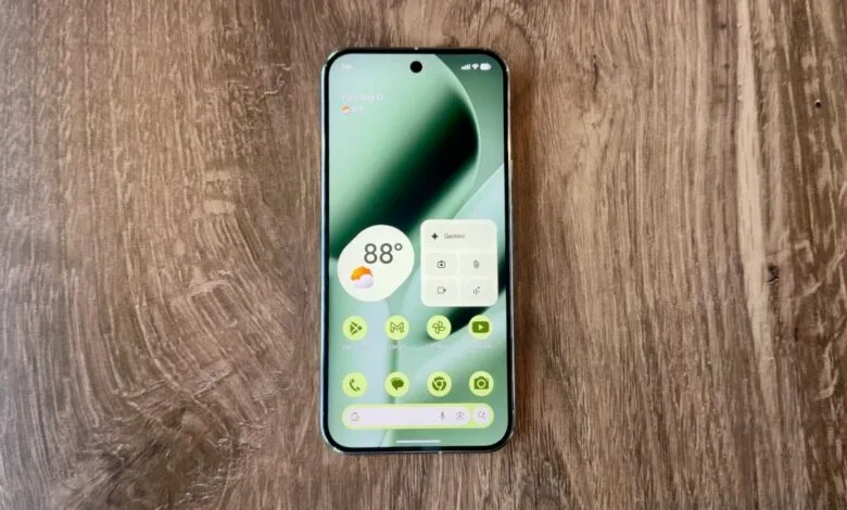 A modern smartphone displaying a green abstract wallpaper and app icons on a wooden surface.