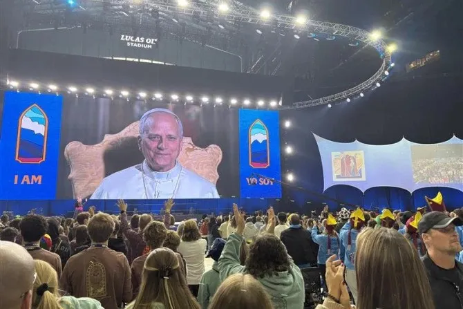 Archbishop Thompson on screen addressing large crowd at Lucas Oil Stadium.