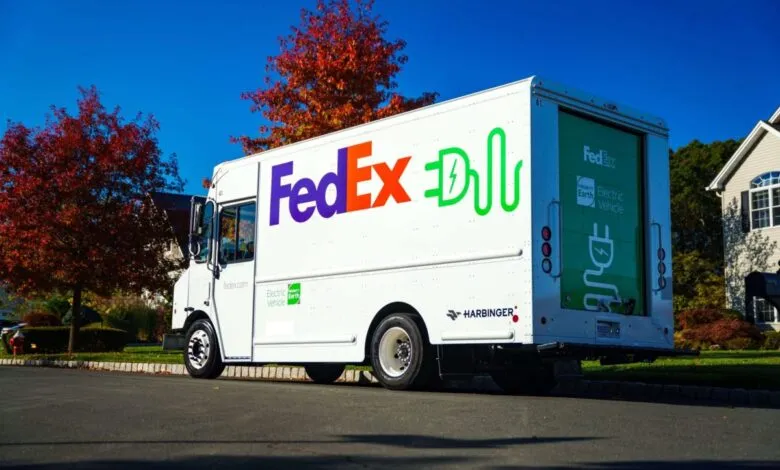 FedEx electric delivery truck with green charging plug logo parked on a suburban street.