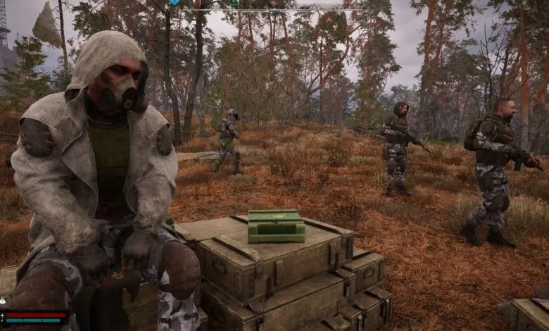 A lone figure in a gas mask and hooded coat sits on crates, while other armed individuals patrol a desolate forest.