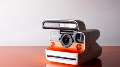 Polaroid camera with orange and white design, flash extended.