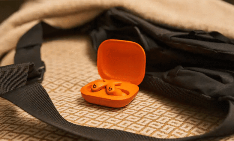 Orange Beats earbuds in open case on patterned surface near black backpack.