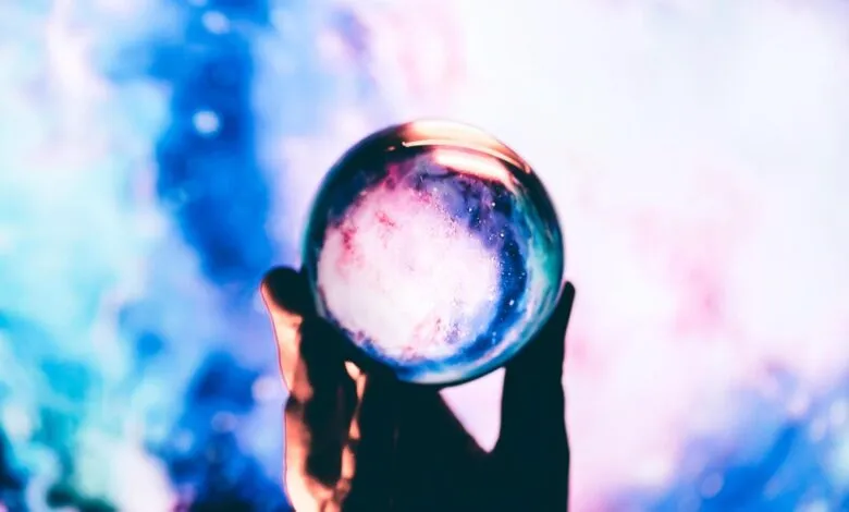 Hand holding crystal ball with galaxy inside against colorful background.