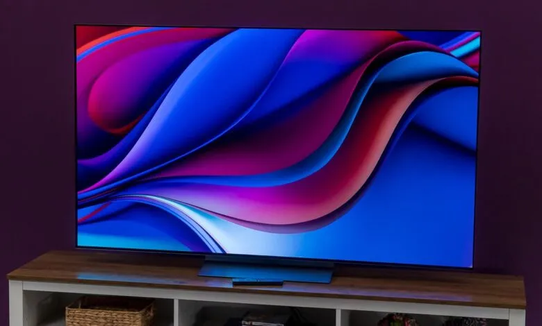 OLED TV displays vibrant abstract art on a wooden media console.