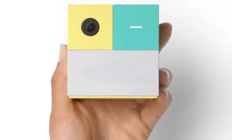 Hand holding a colorful, cube-shaped camera with a lens.