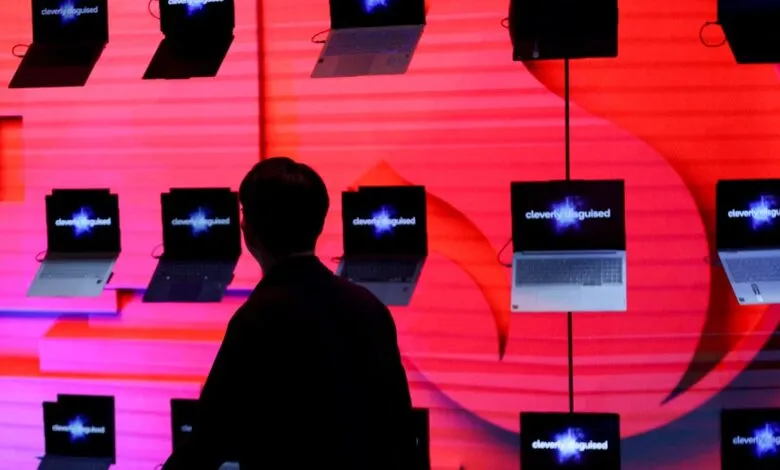 Display of laptops with 'cleverly disguised' text on screens, person in foreground.