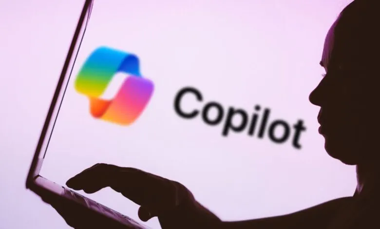 Silhouette of person using laptop displaying the Copilot logo.