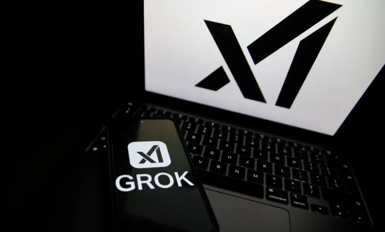 Phone displaying the Grok logo sits on a laptop with the X logo on the screen.