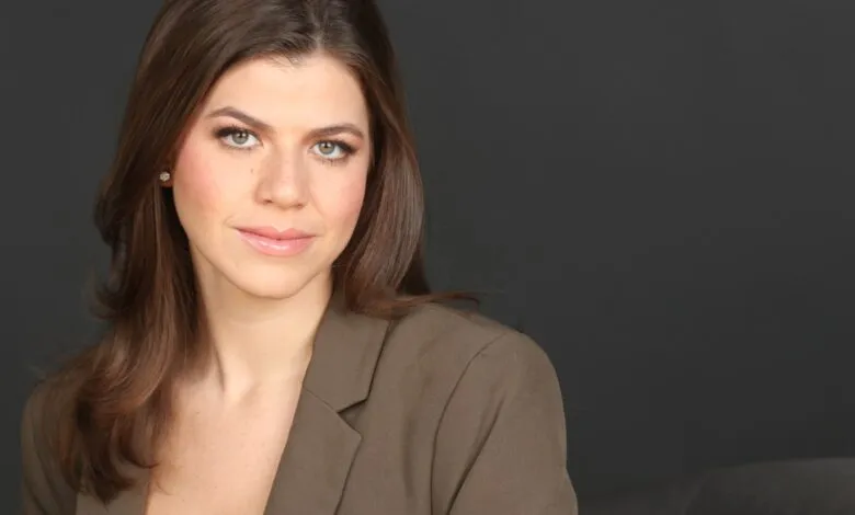 Professional headshot of a woman with brown hair and a blazer against a gray background.