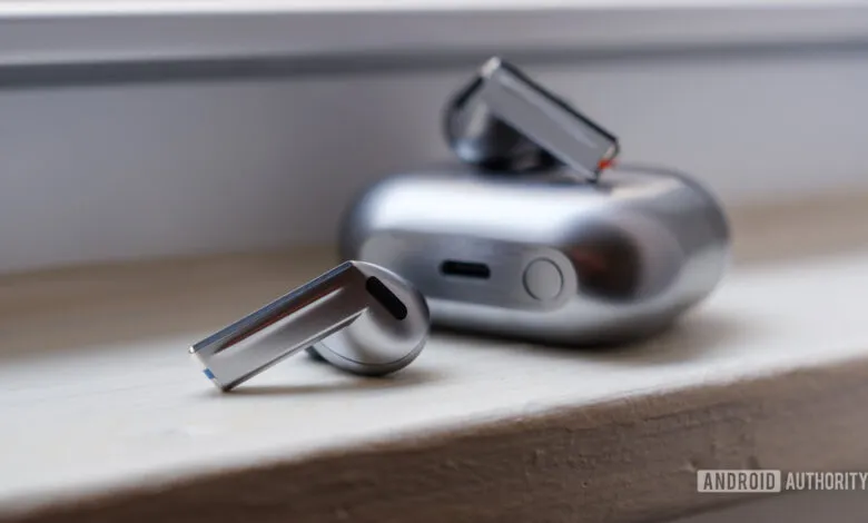 Close-up of silver wireless earbuds and charging case on a windowsill.