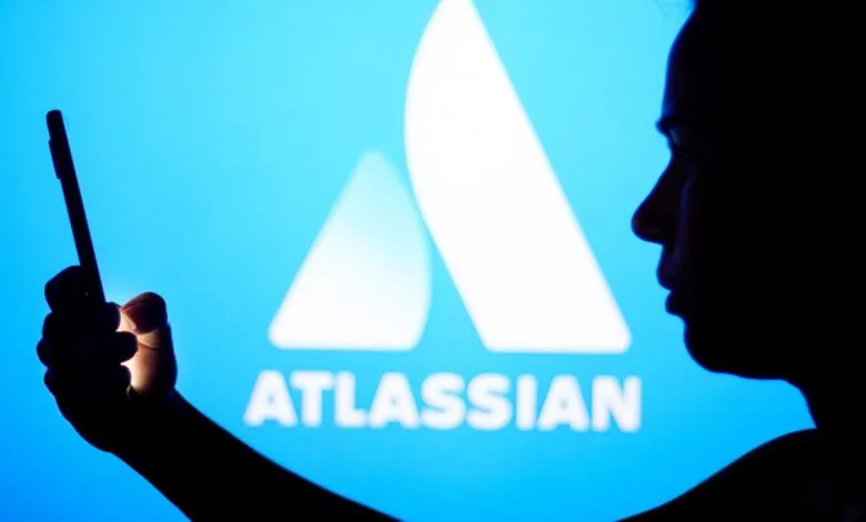 Silhouette of person using phone in front of Atlassian logo on blue screen.