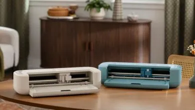 Two Cricut Joy cutting machines, one white and one blue, on a wooden table.
