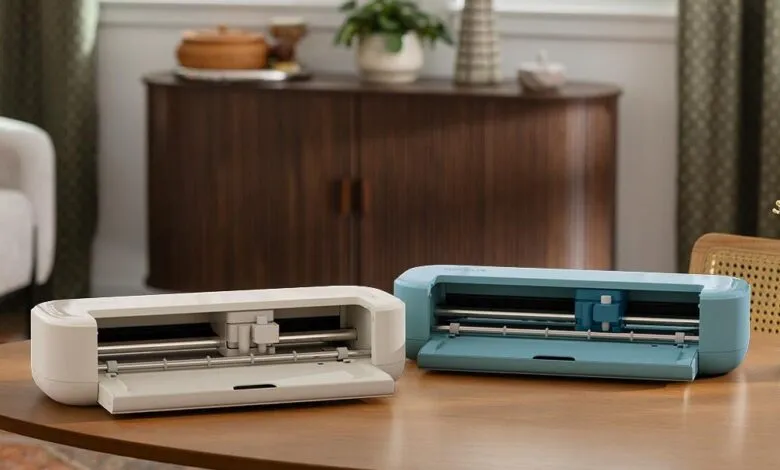 Two Cricut Joy cutting machines, one white and one blue, on a wooden table.