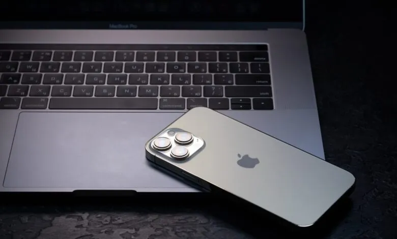 Apple iPhone 15 Pro rests on a Macbook Pro laptop, showcasing modern tech.