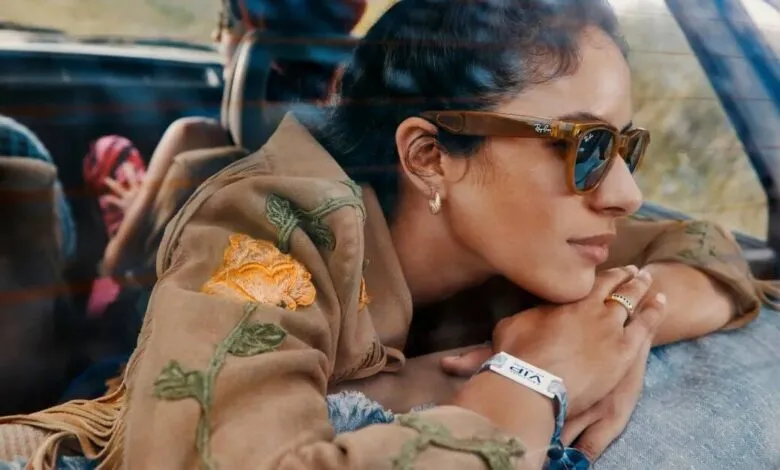 Woman in Ray-Ban sunglasses leans in car, wearing floral jacket.