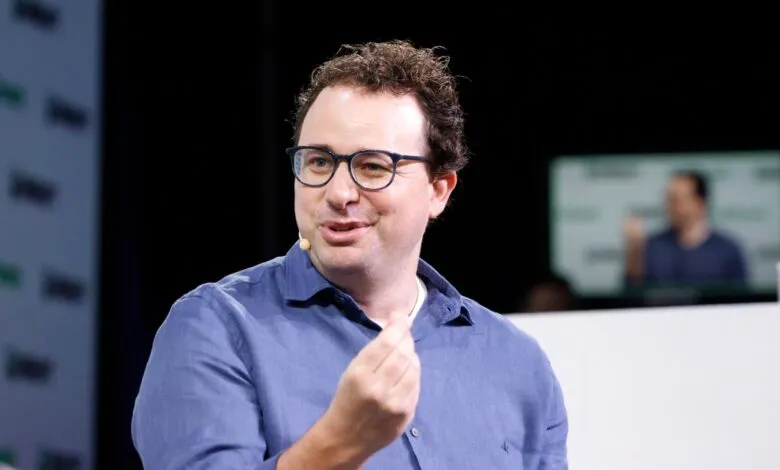 Man with glasses gestures during a presentation on stage.