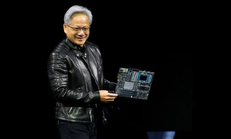 Jensen Huang holds a motherboard, smiling against a dark background.