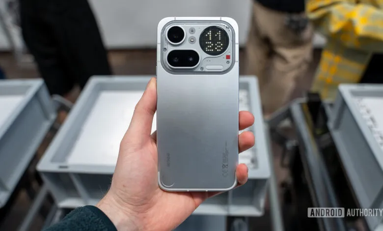 Hand holding a silver Nothing Phone with unique camera design.