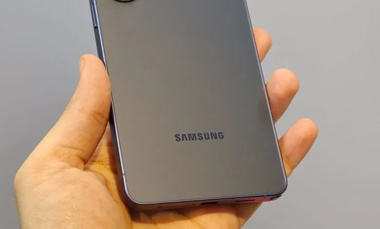Hand holding a gray Samsung smartphone, back view.