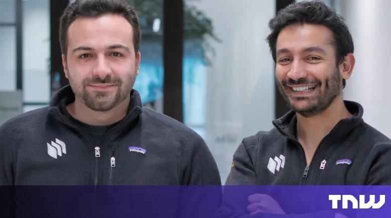 Two smiling men stand side-by-side in matching gray zip-up sweaters.