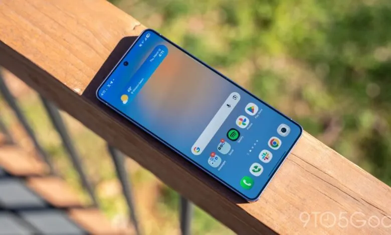 Smartphone displaying home screen resting on wooden railing outdoors.