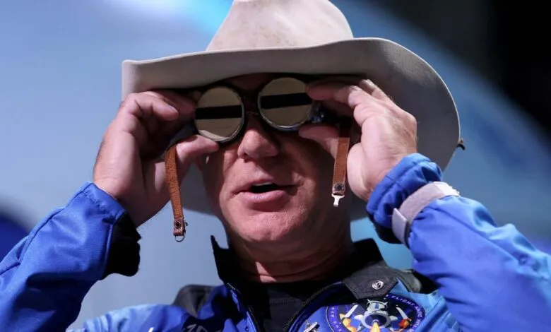 Jeff Bezos adjusts goggles, wearing cowboy hat and blue spacesuit.