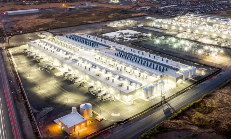 Aerial view of a large data center complex at night, brightly lit.