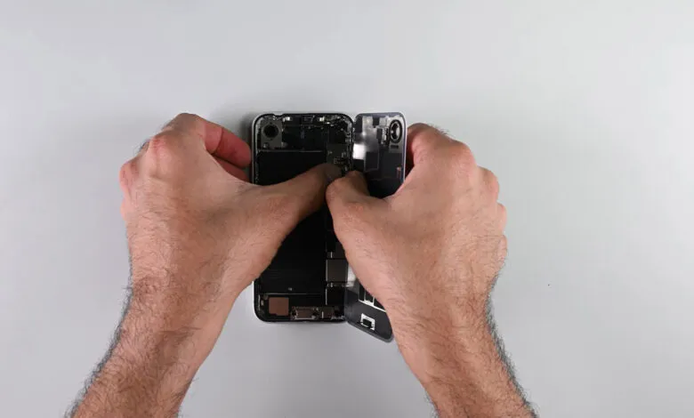 Hands carefully open a smartphone, revealing its internal components.