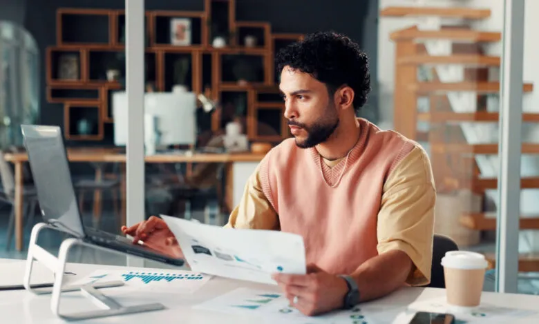 Man works at desk with laptop and charts in modern office space.