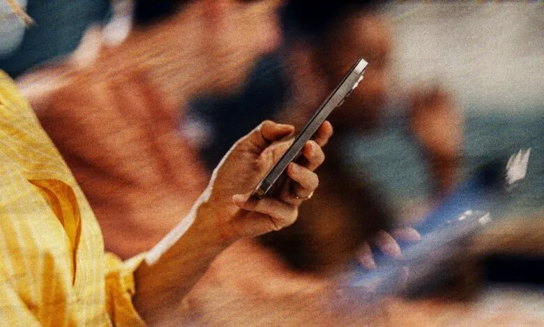 Person in yellow shirt holds silver smartphone in their hand.