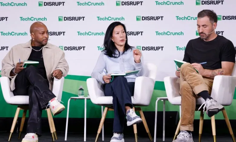 Three panelists sit on stage at TechCrunch Disrupt, taking notes.