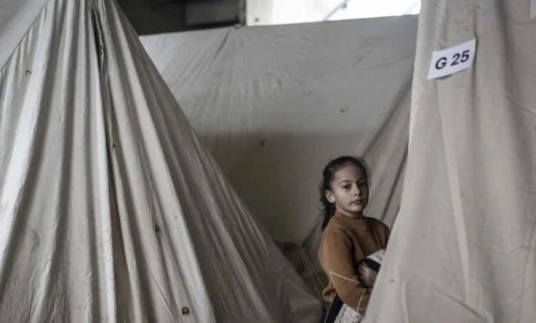 Young girl stands in tent with 'G 25' label, looking at camera.