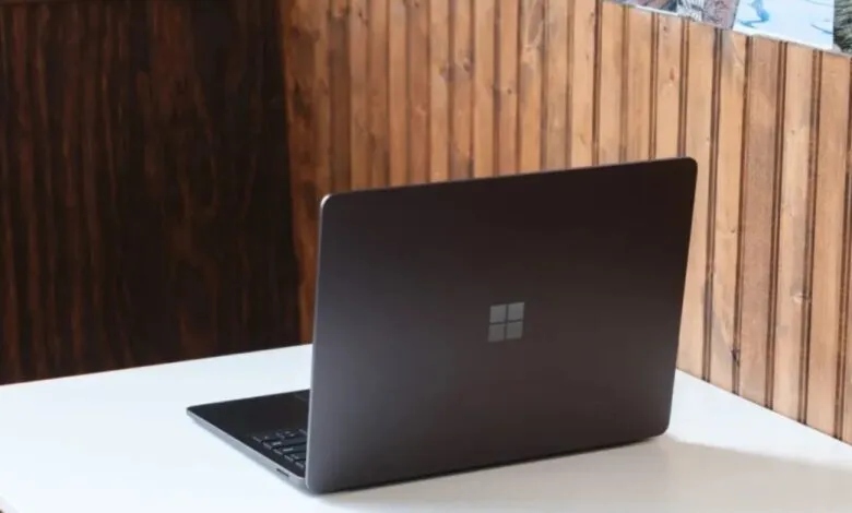 Dark grey Microsoft Surface Laptop on white desk with wood panel background.