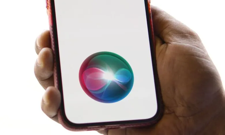 Hand holding iPhone with Siri interface displayed on screen.