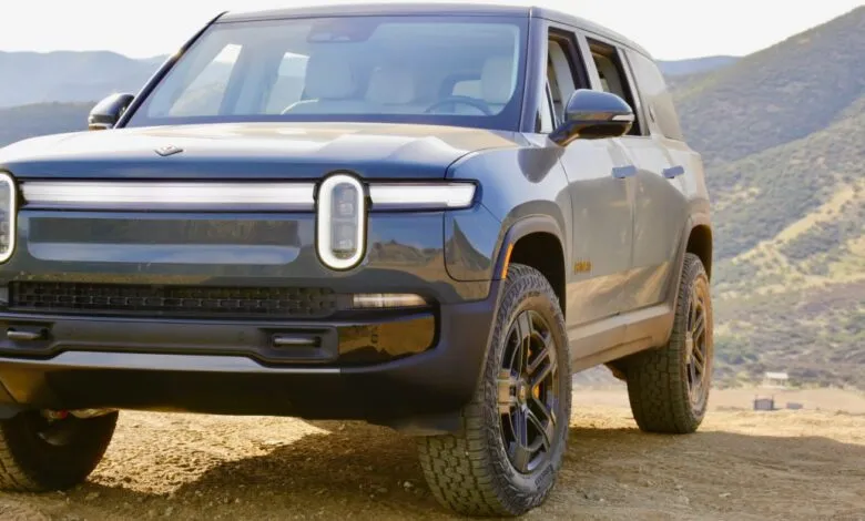 Rivian R1S electric SUV parked on a dirt road with mountains in the background.