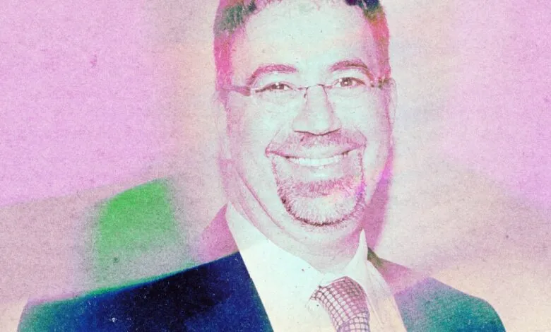 Smiling man with glasses and a suit, filtered with pink and blue hues.