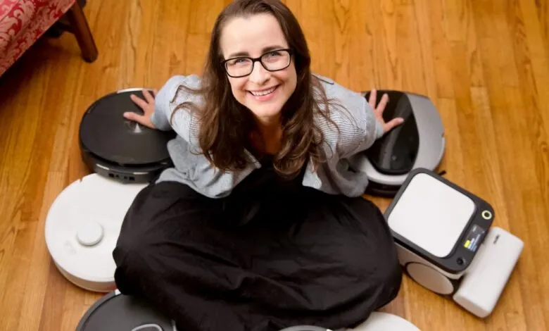 Woman smiling surrounded by various robot vacuum cleaners on wood floor.