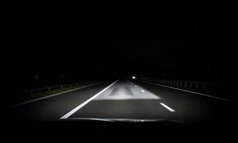Nighttime view of a highway illuminated by car headlights.