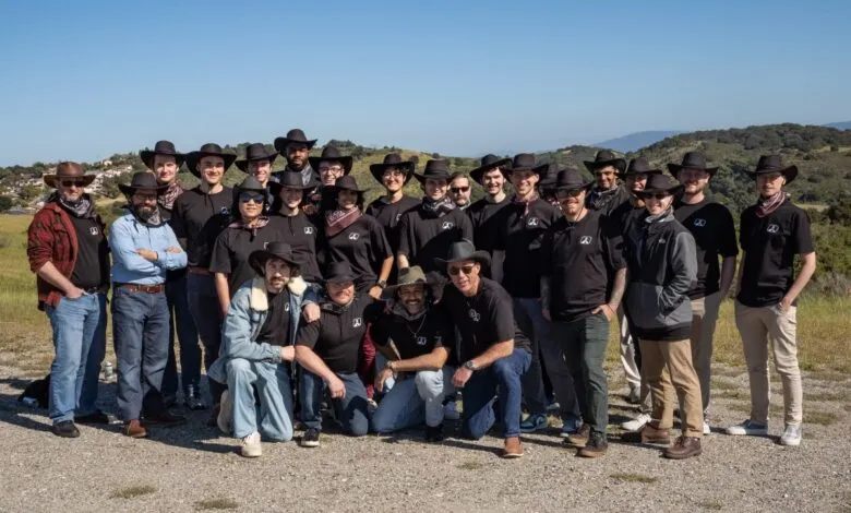 Group of about 25 people wearing cowboy hats and matching shirts posing outdoors.