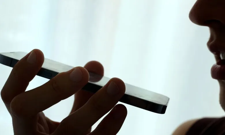 Person using voice assistant on smartphone, close-up silhouette.