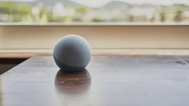 Round blue smart speaker on a polished wooden table near a bright window.