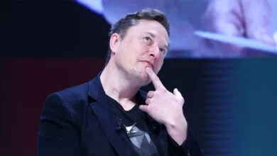 Elon Musk thoughtfully poses with finger on chin.