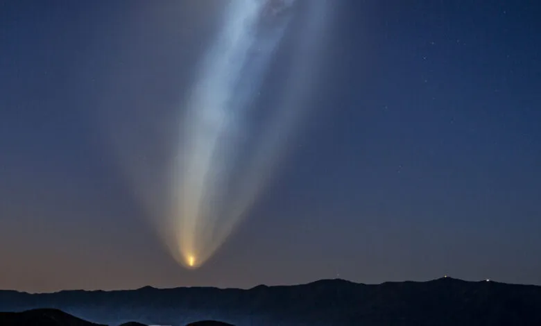 Rocket launch creates bright plume in night sky above dark mountains.