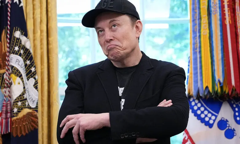 Elon Musk with arms crossed, wearing a black baseball cap.