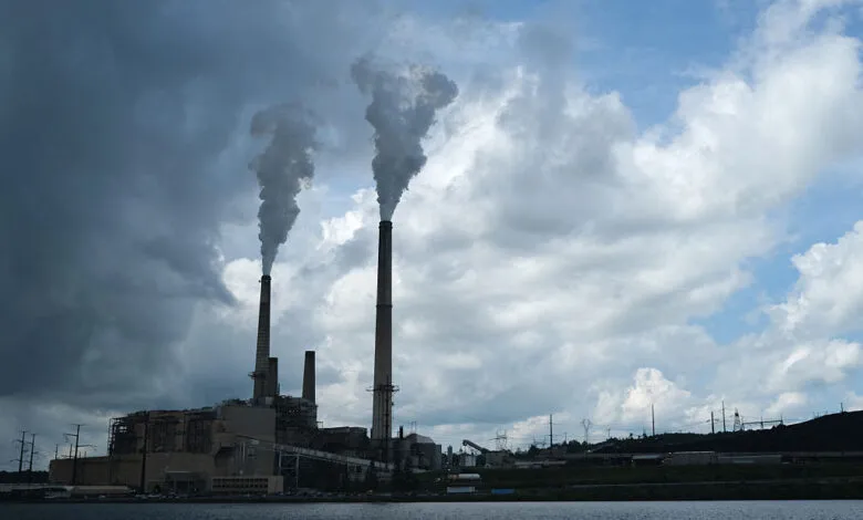 Coal-fired power plant with smokestacks emitting plumes against a cloudy sky.