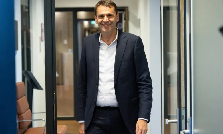 Smiling man in suit walks through office doorway.
