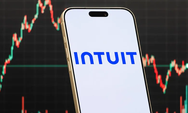 Smartphone displays Intuit logo against stock market chart background.