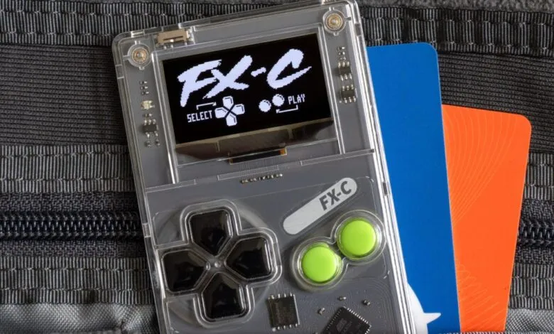 Clear Arduboy FX-C handheld game console with credit cards.